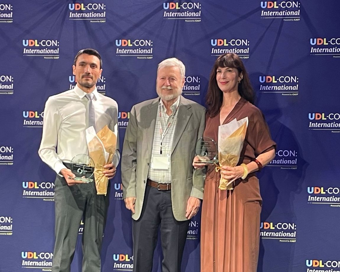 Soldan sağa: Jérémie Rostan, David Rose ve Beth Stark, UDL-CON: International'da. Rostan ve Stark, Rose'un iki yanında, lacivert bir UDL-CON: International arka planı önünde, her biri birer cam ödül ve buket tutuyor.